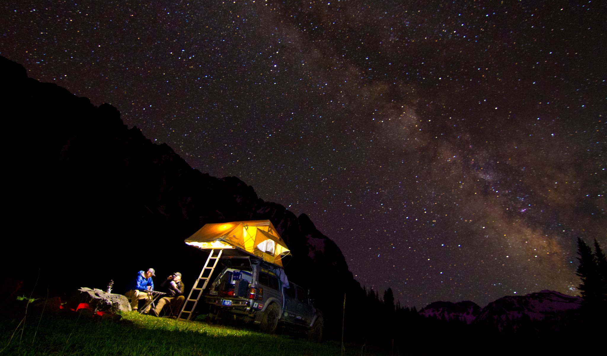 Overland camp under the Milky Way with a lit rooftop tent