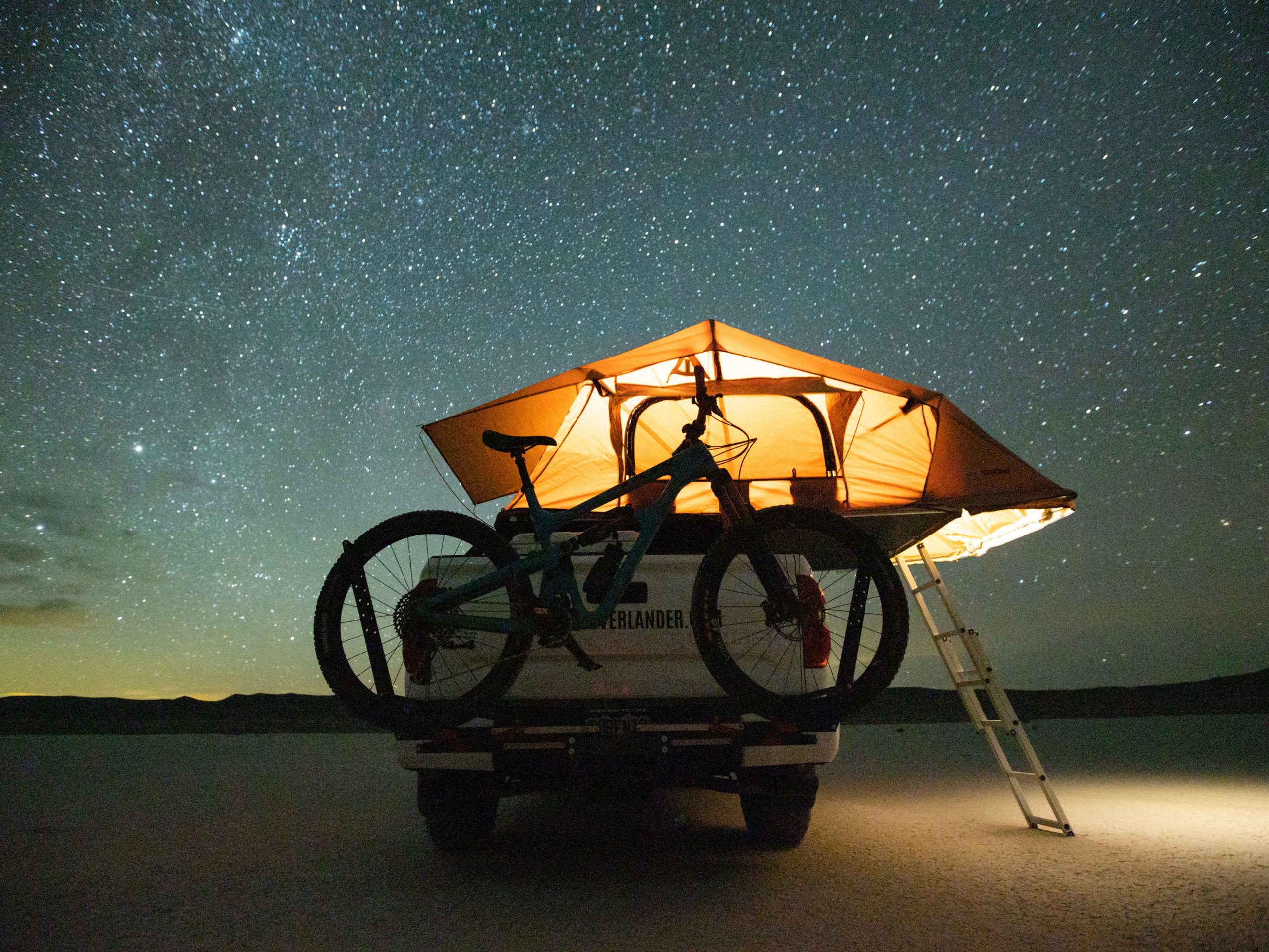Rooftop tent glowing under the stars on an overland pickup